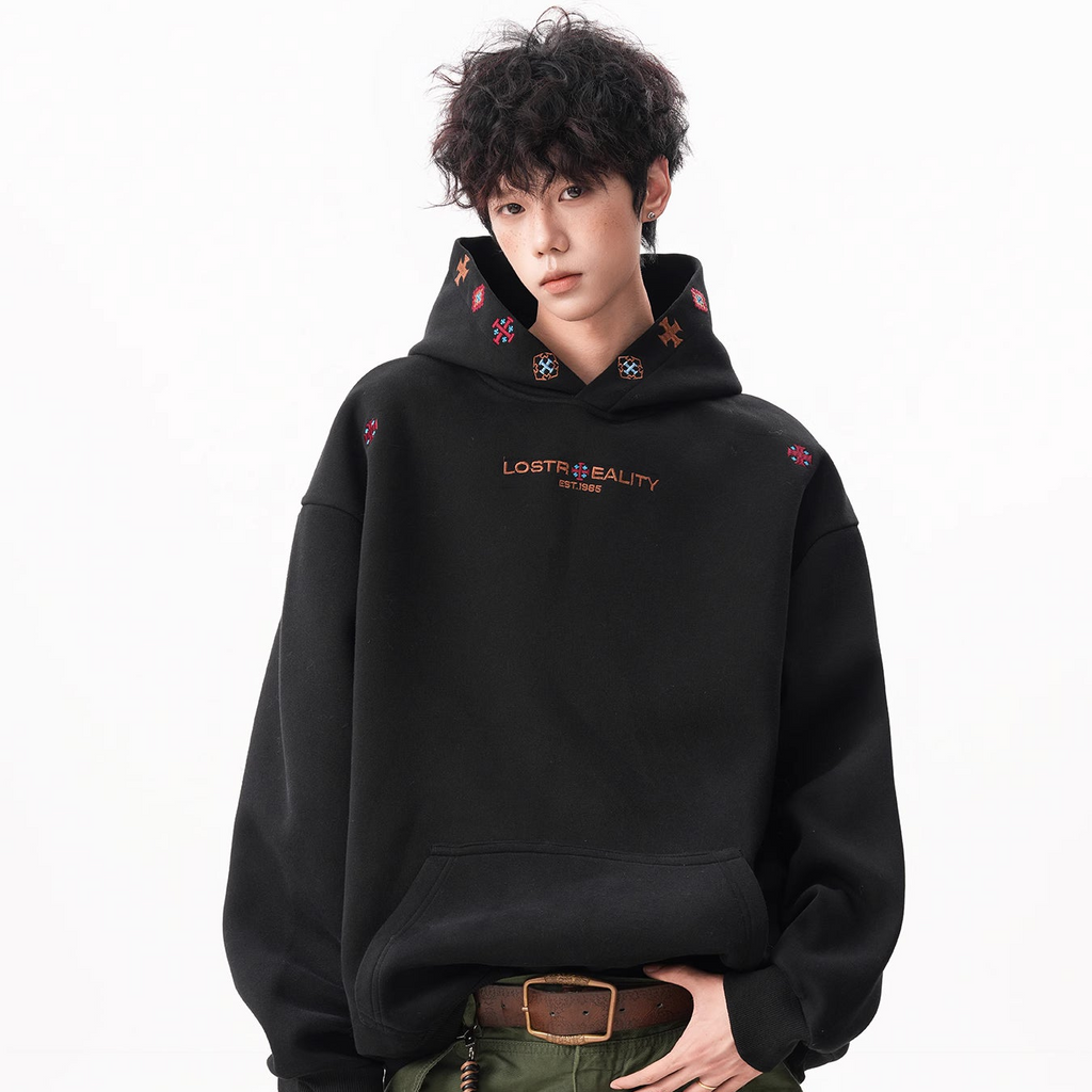 Person wearing a black hoodie with embroidery and green pants on a white background